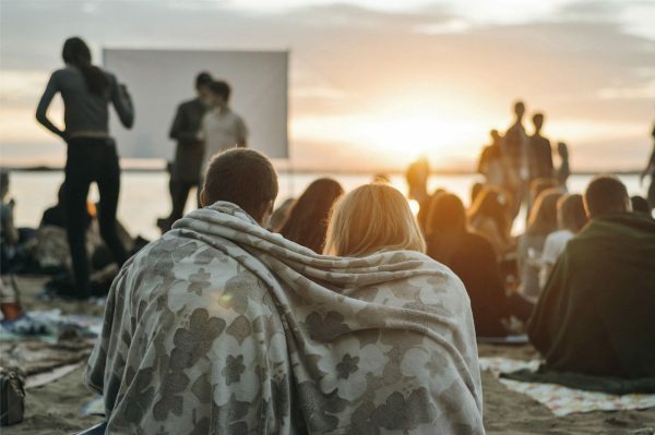People sit to watch a film being projected on a beach.